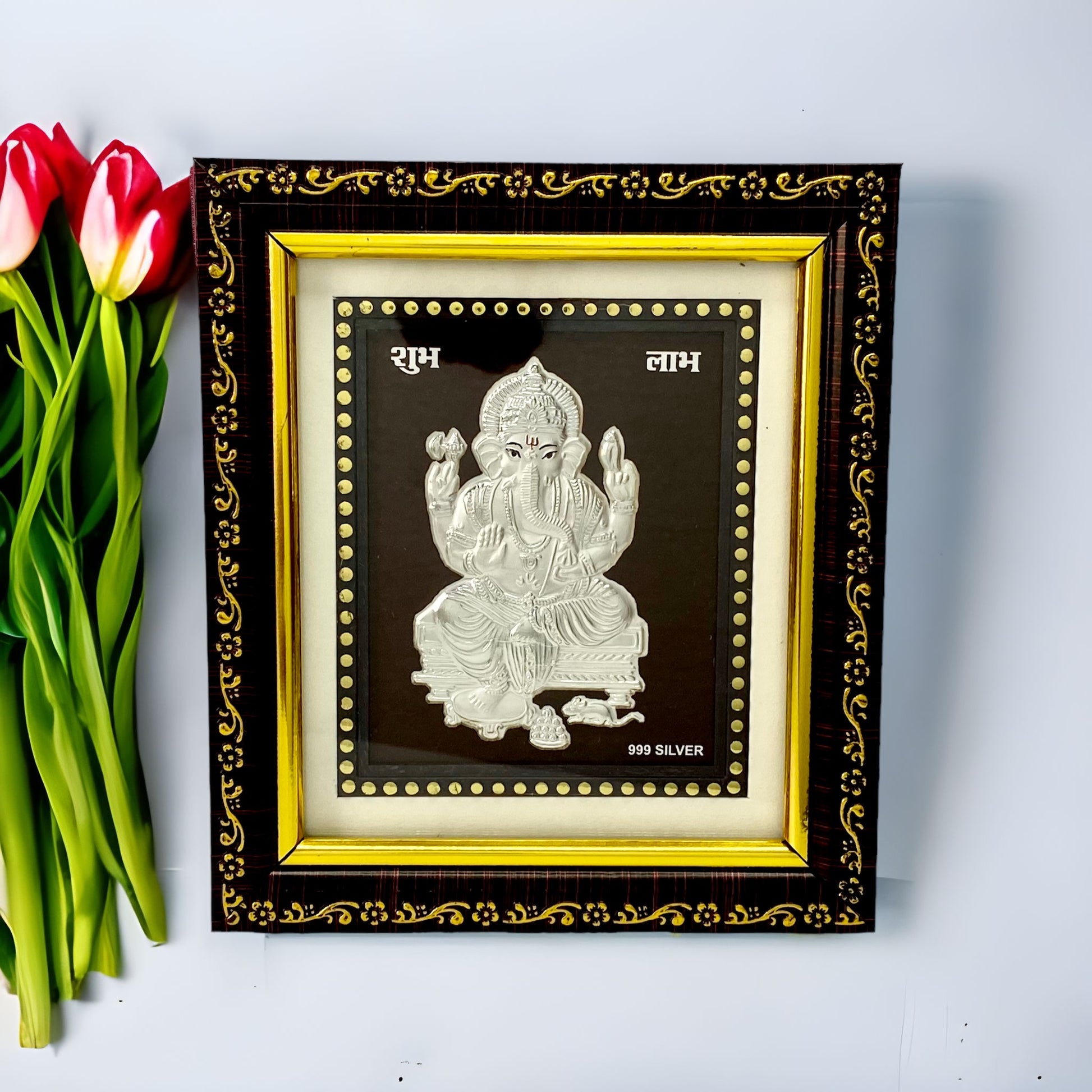 "Front view of pure silver Ganesh frame by Hem Jewels® beautifully adorned with flowers on a table."