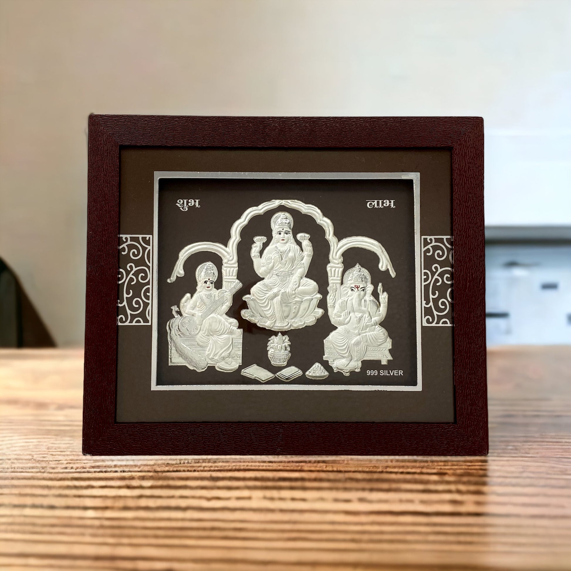 "Front view of pure silver Trimurti (Laxmi Ganesh Saraswati) frame by Hem Jewels® placed on a table."	