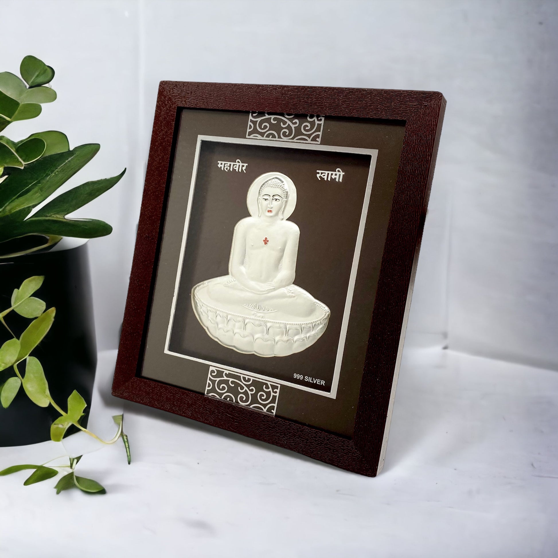 "Angled view of the pure silver Mahaveer frame by Hem Jewels® placed on a wooden table."	