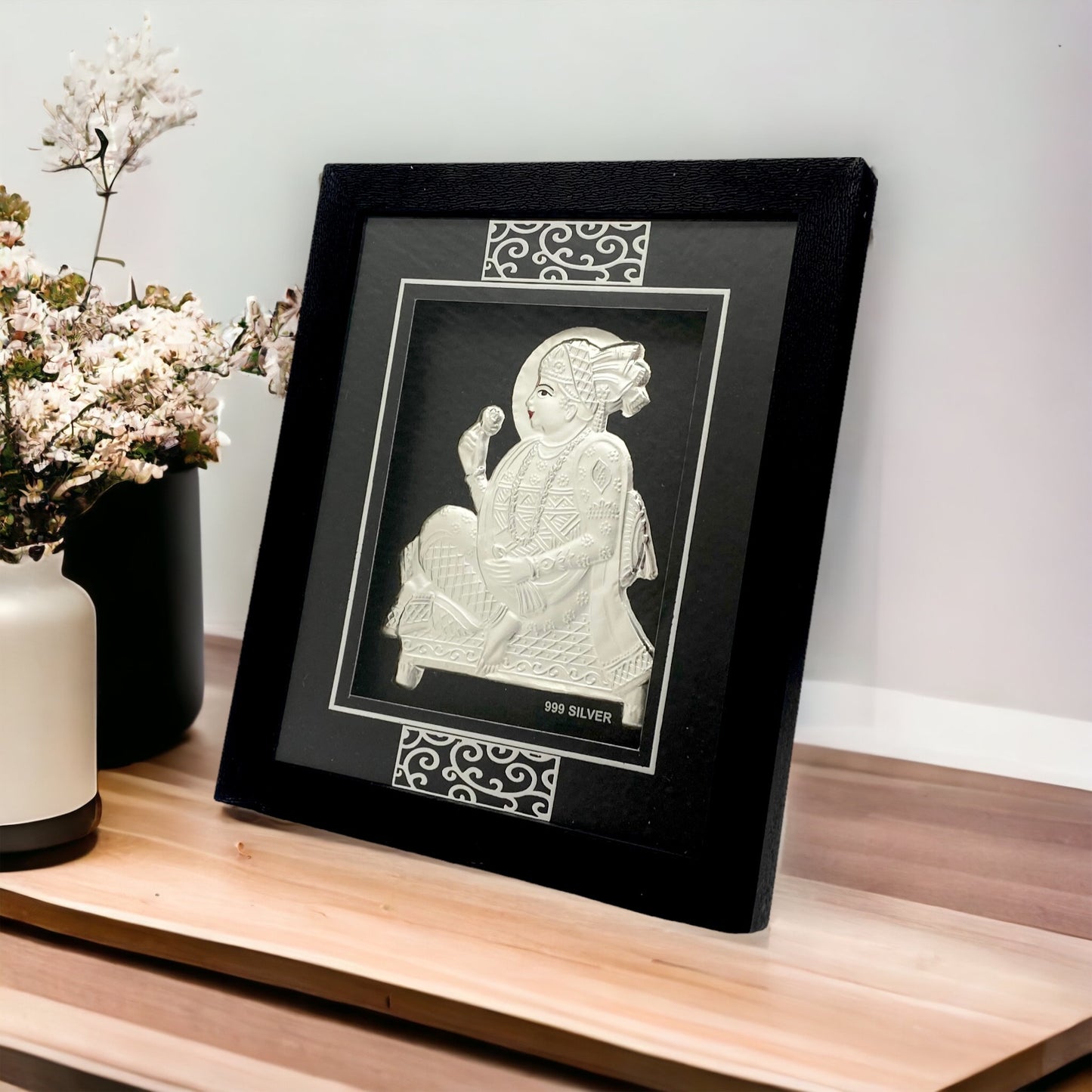 "Angled view of the pure silver Swaminarayan frame by Hem Jewels® placed on a wooden table."	